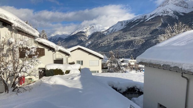 Ein Wohngebiet mit schneebedeckten Dächern und Bergen im Hintergrund.