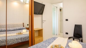 Een slaapkamer met een bed, een aan de muur bevestigde televisie, een stoel en een klein tafeltje met kopjes.