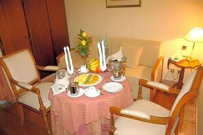 A dining table set with plates, glasses, and a fruit bowl, surrounded by chairs. - Jardim Hotel (Santo Tirso)