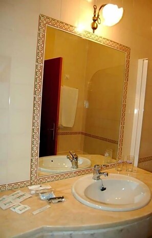 A bathroom with a large mirror, a sink, and toiletries on the counter. - Jardim Hotel (Santo Tirso)