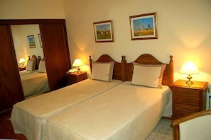A double bed with a wooden headboard, two bedside tables with lamps, a mirror, and two framed pictures on the wall. - Jardim Hotel (Santo Tirso)