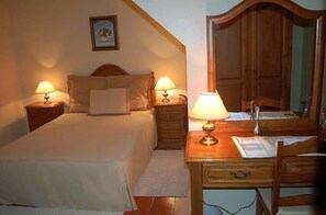 Un dormitorio con cama, dos mesitas de noche con lámparas, un escritorio de madera con una silla y un espejo.