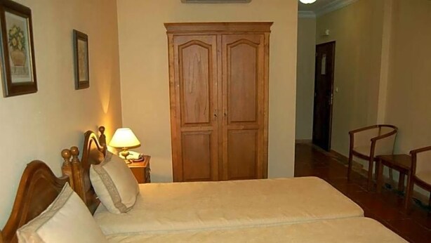 Een slaapkamer met een bed, een houten garderobe, een nachtkastje met een lamp en een stoel.