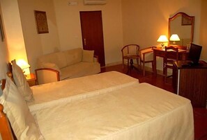 A hotel room with a bed, a sofa, a desk with a chair, a lamp, and a mirror. - Jardim Hotel (Santo Tirso)