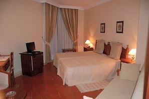 A hotel room with a bed, bedside tables, a desk, a chair, a TV, and curtains. - Jardim Hotel (Santo Tirso)