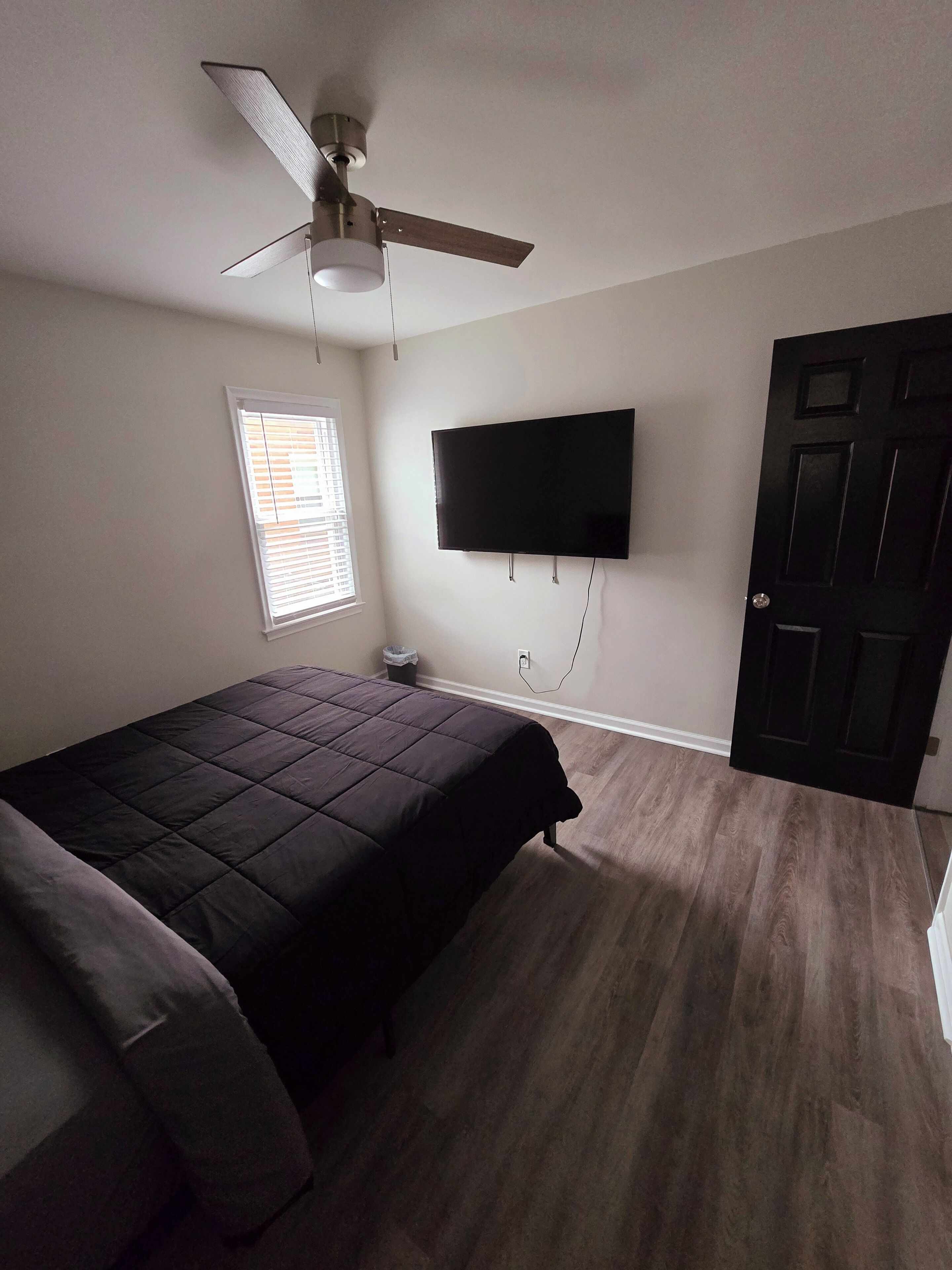 A bedroom with a bed, ceiling fan, TV, window, and door.