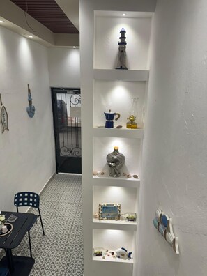 Ein Zimmer mit weißer Wand, einem Regal mit Dekoration, einem gemusterten Boden und einer Tür mit Metallgitter.