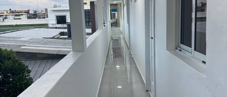 A corridor with white walls, a tiled floor, and a window on the right.