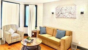 Een woonkamer met een gestreept fauteuil, een beige bank met blauwe kussens, een ronde salontafel en een schilderij aan de muur.