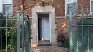 Een bakstenen gebouw met een dubbele deur, een klein tuin met potplanten en een metalen hek.