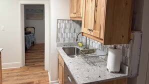 A kitchen with wooden cabinets, a granite countertop, a tiled backsplash, and a visible dining area. - MedCity Suite—2BR/1BA Near Mayo Clinic (Rochester)