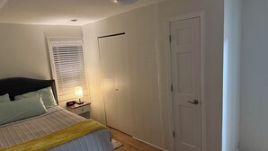 A bedroom with a bed, bedside table with lamp, window with blinds, and a door. - MedCity Suite—2BR/1BA Near Mayo Clinic (Rochester)
