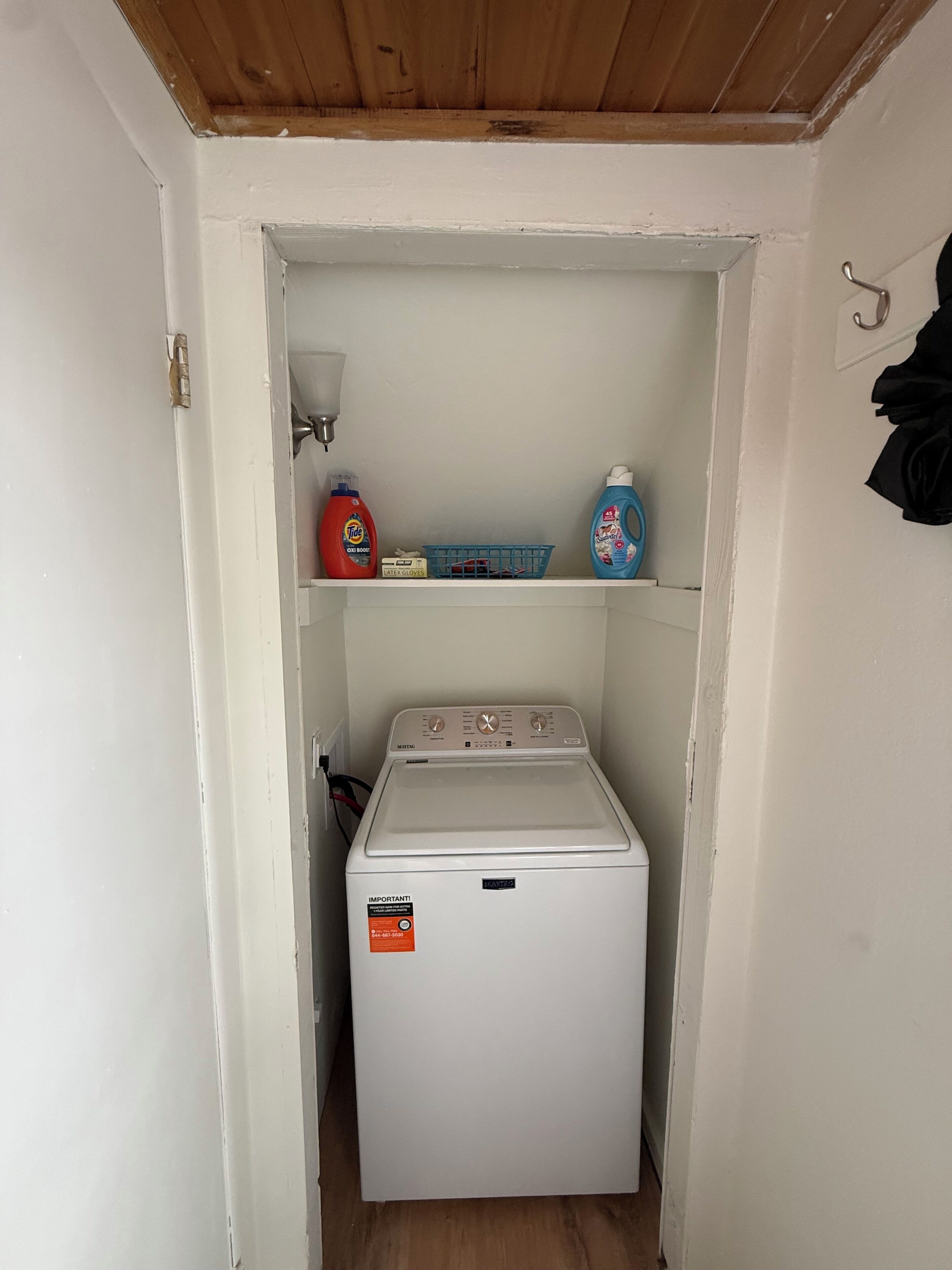 A laundry room with a washing machine, detergent, and a basket.