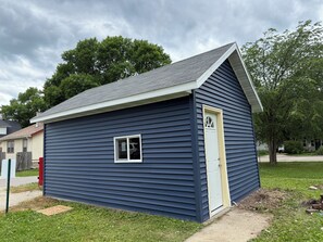 A small, single-story building with a dark blue exterior, a white door, and a small window. - MedCity Suite—2BR/1BA Near Mayo Clinic (Rochester)