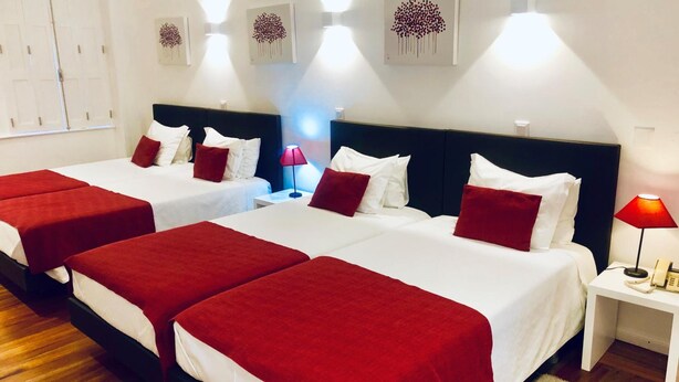 Ein Hotelzimmer mit zwei Betten, jeweils mit weißer Bettwäsche und roten Akzenten, einem Nachttisch mit Lampe sowie Bildern an den Wänden.