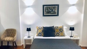 Ein ordentlich eingerichtetes Schlafzimmer mit einem Bett, zwei Nachttischen, einem Sessel und einem Wandbild.