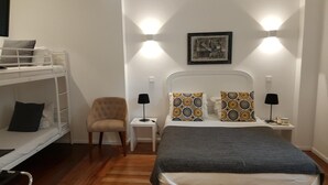 Ein Stockbett mit Stuhl und Nachttischen, ein Bett mit gemusterten Kissen und eine Wandleuchte.