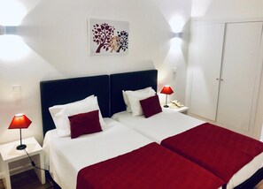 A double bed with white and red bedding, two bedside tables with lamps, a wardrobe, and a wall-mounted artwork. - Hotel Botanico de Coimbra (Barcelos)