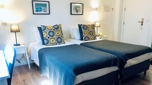 Una cama doble con almohadones estampados, una mesita de noche con lámpara y un teléfono en la pared.