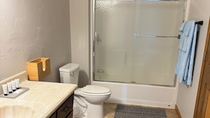 Et badeværelse med toilet, vask, brusebad og et håndklædetørrestativ.