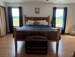 A bedroom with a wooden bed, a nightstand, a lamp, and a suitcase. - Spacious 5-bedroom house ideal for families or fishing groups (Roosevelt)