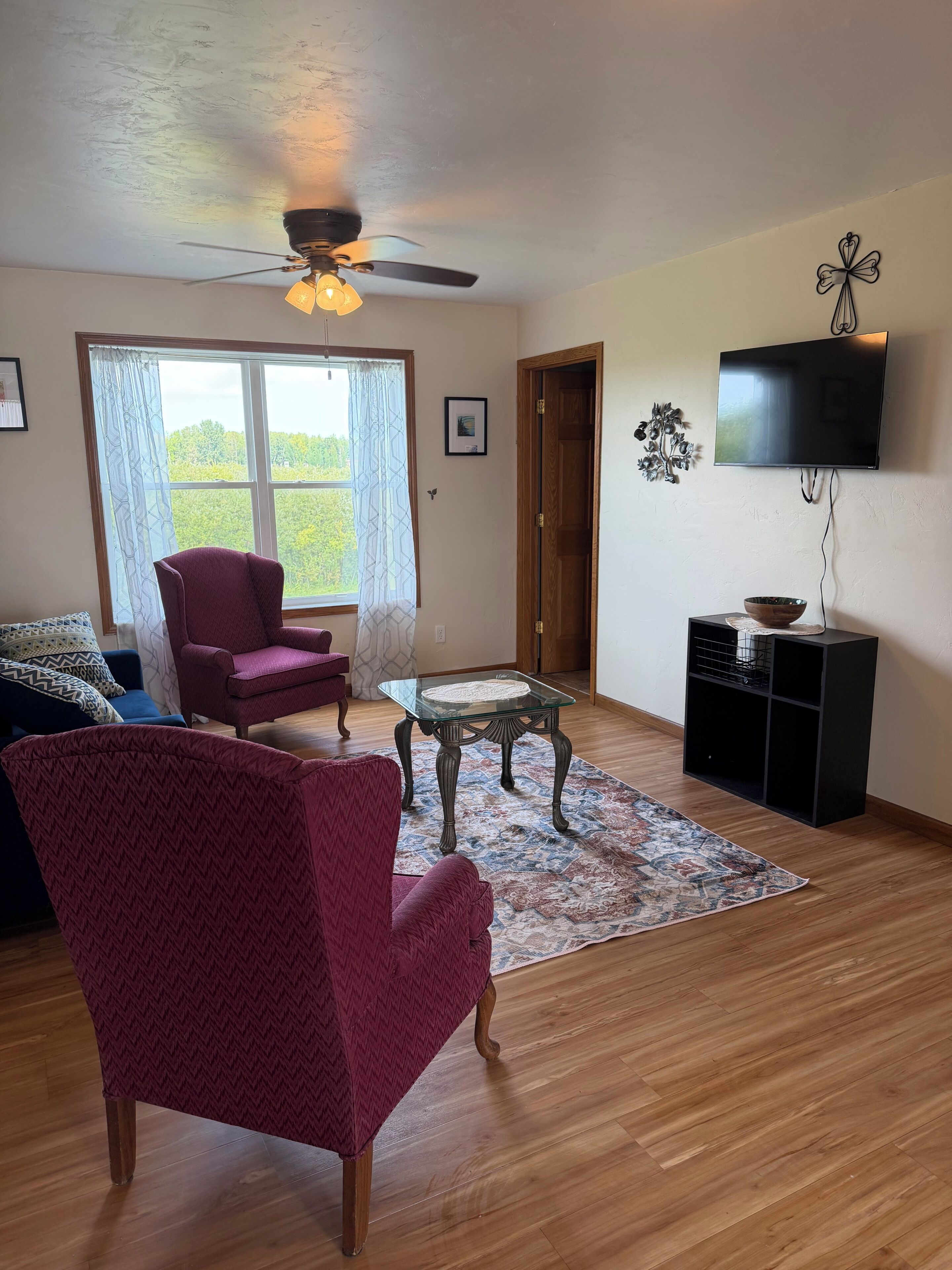 A living room with a ceiling fan, a television, a glass coffee table, and a patterned rug.