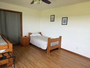 A bedroom with a single bed, a nightstand, a wooden dresser, and a ceiling fan.