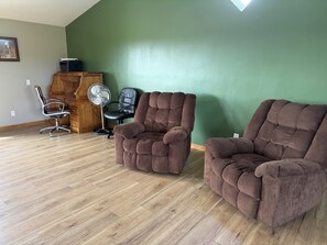 A room with two brown armchairs, a wooden desk, a black office chair, and a standing fan.