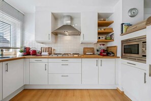 A modern kitchen with white cabinets, a wooden countertop, a stainless steel range hood, a microwave, and a clock on the wall. - 0 bedroom accommodation in OOSTENDE (OOSTENDE)
