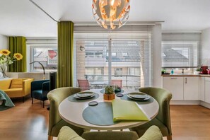 A modern living room with a dining table, green curtains, a yellow sofa, and a view of the city through large windows. - 0 bedroom accommodation in OOSTENDE (OOSTENDE)
