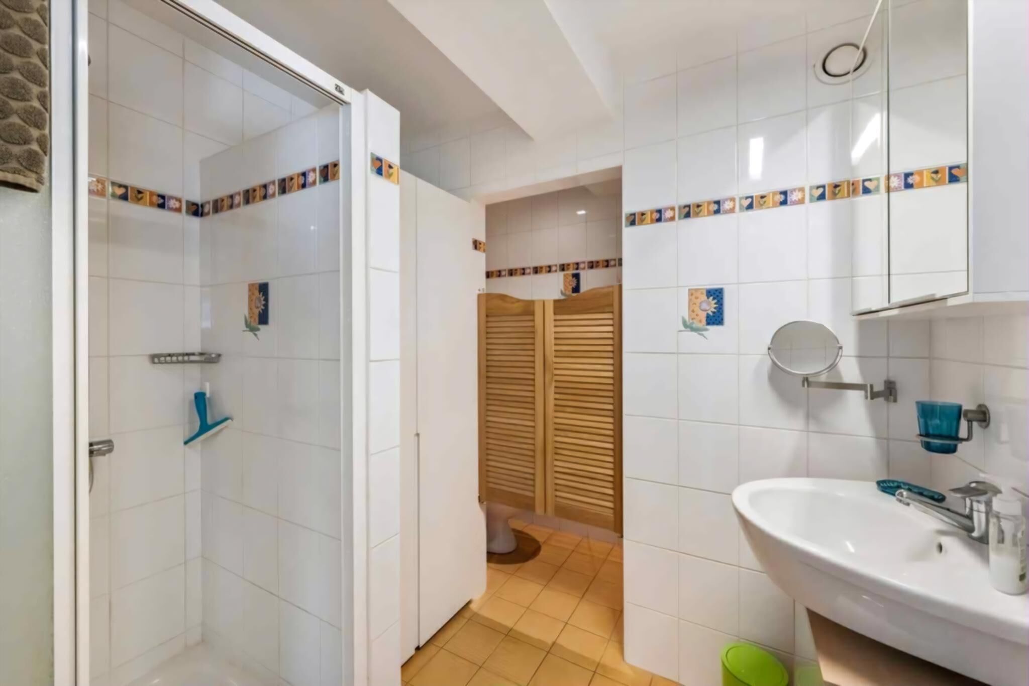 Une salle de bain équipée d’une douche, de toilettes et d’un lavabo, avec des murs carrelés et une porte en bois.