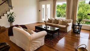 A spacious living room with a wooden floor, a sofa set, a coffee table, and a staircase.