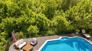 A swimming pool with a wooden deck, lounge chairs, and a pink umbrella.