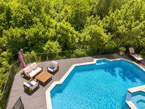 A swimming pool with a wooden deck, lounge chairs, and a pink umbrella.