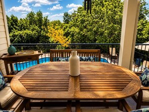 A round wooden table with a vase, surrounded by chairs with cushions, overlooking a swimming pool. - Hill Country Oasis with Pool, Spa & Views (Austin)