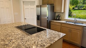 A kitchen with granite countertops, stainless steel appliances, wooden cabinets, and a window with a view of greenery.