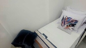 A single bed with a striped blanket, a pillow with a feather pattern, and a remote control on the bed.