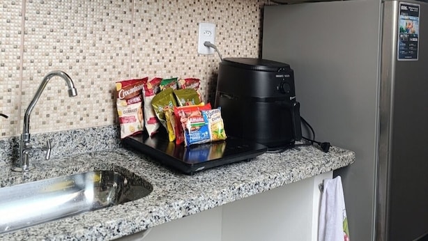 A kitchen with a granite countertop, a stainless steel refrigerator, a coffee maker, and a variety of packaged food items.