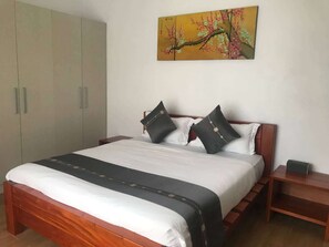A bedroom with a bed, pillows, a nightstand, a wardrobe, and a painting on the wall.