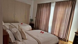 A double bed with a patterned bedspread, a wardrobe, and a window with curtains. - Villa 61 of Naisoso island (Nadi)