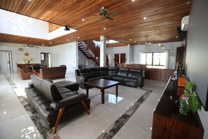 Amplia sala de estar con techo de madera, un sofá de cuero negro, una mesa de centro y una escalera que conduce a otro nivel.