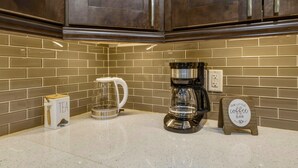 Cucina con pensili in legno scuro, una macchina per caffè, un bollitore e un cartello con scritto 'Il nostro piccolo caffè'.