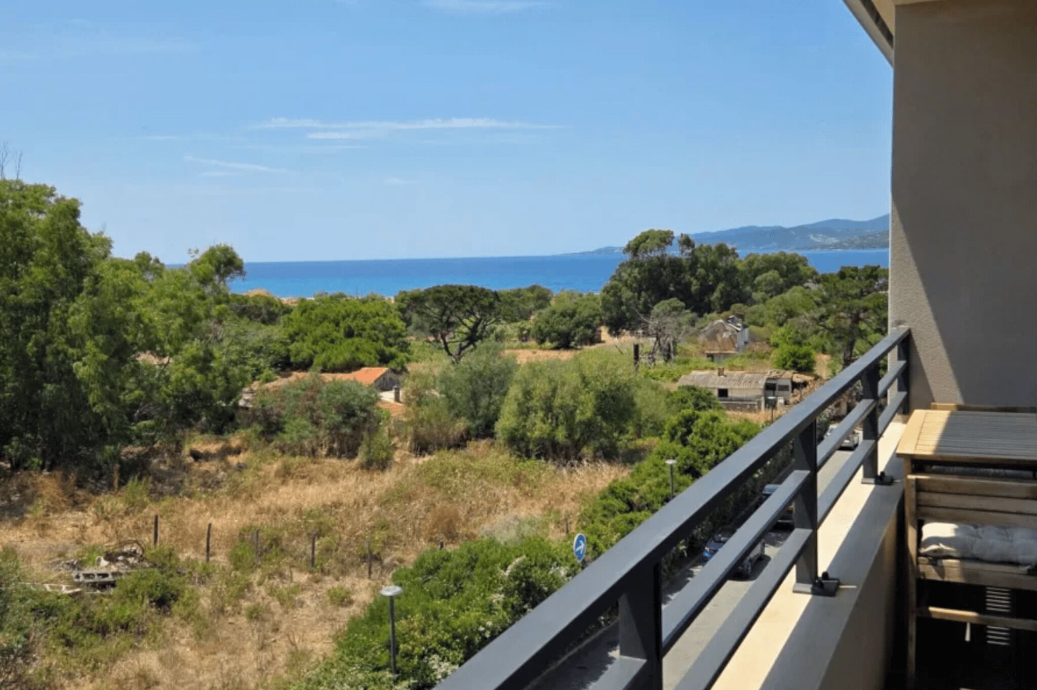 Un balcon offrant une vue sur un paysage côtier, avec des arbres et une étendue d’eau visible au loin.