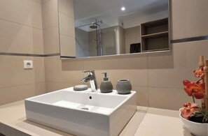 Ein Badezimmer mit einem großen Spiegel, einem weißen Waschbecken, einer Dusche und einem Blumentopf.