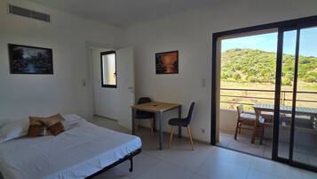 Une chambre avec un lit, un bureau et une chaise, un balcon avec une table et des chaises, et deux tableaux accrochés aux murs.