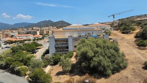 Un edifici amb diverses plantes, una grua de construcció i un paisatge amb turons i vegetació escassa.