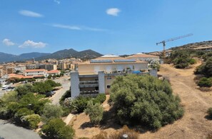 Ein mehrstöckiges Gebäude, ein Turmdrehkran und eine hügelige Landschaft mit spärlicher Vegetation.