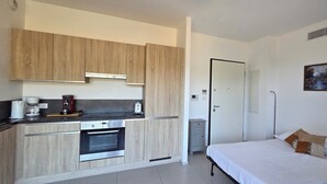 Habitació petita amb cuineta, un llit i un quadre a la paret.