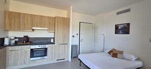 Ein kleines Zimmer mit einer Küchenzeile, einem Bett und einem Bild an der Wand.