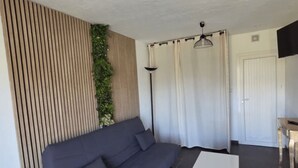 En moderne stue med en mørkegrå sofa, et hvidt sofabord, en gulvlampe samt en væg med lodrette trælameller og en grøn plante.